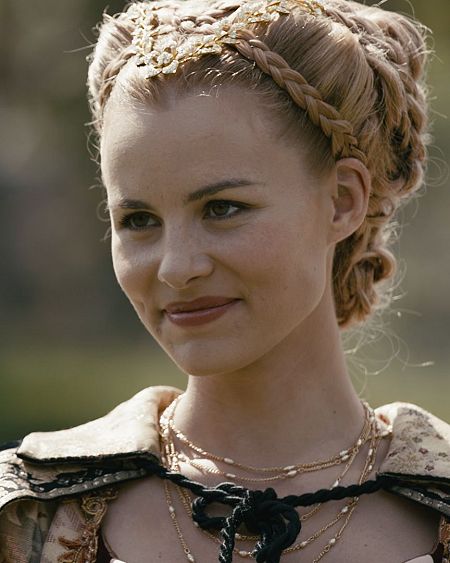 Olivia Molina interpreta a la reina María en esta imagen promocional, luciendo un elegante vestido de época y un peinado recogido.