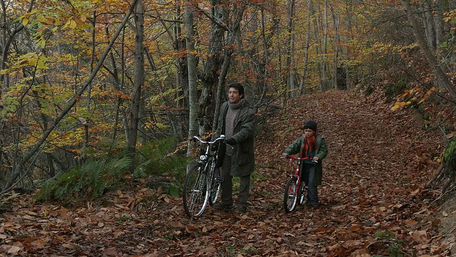 José Luis Cuerda y un niño con bicicletas en un bosque otoñal, escena de 'La educación de las hadas'.