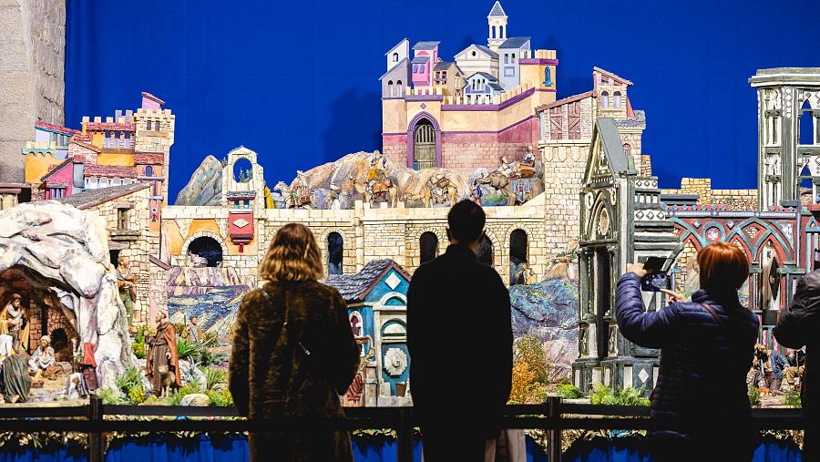 Visitantes observan el pesebre navideño de la Asociación de Pessebristes de Barcelona, con figuras y edificaciones detalladas.