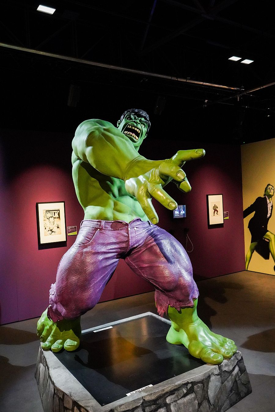 Figura gigante de Hulk en una exposición, con pose agresiva y pantalones morados.