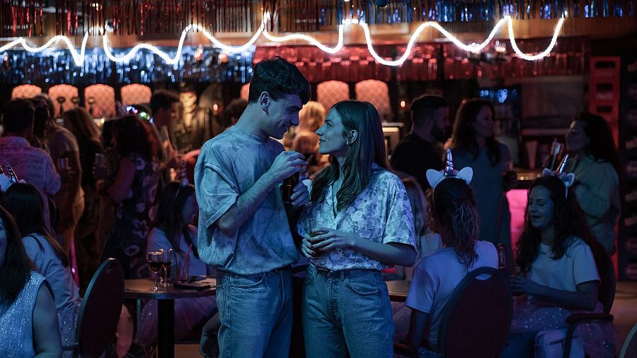 Àlex Monner y Marina Salas se miran en un bar lleno de gente en una escena de la película 'El Cover'.
