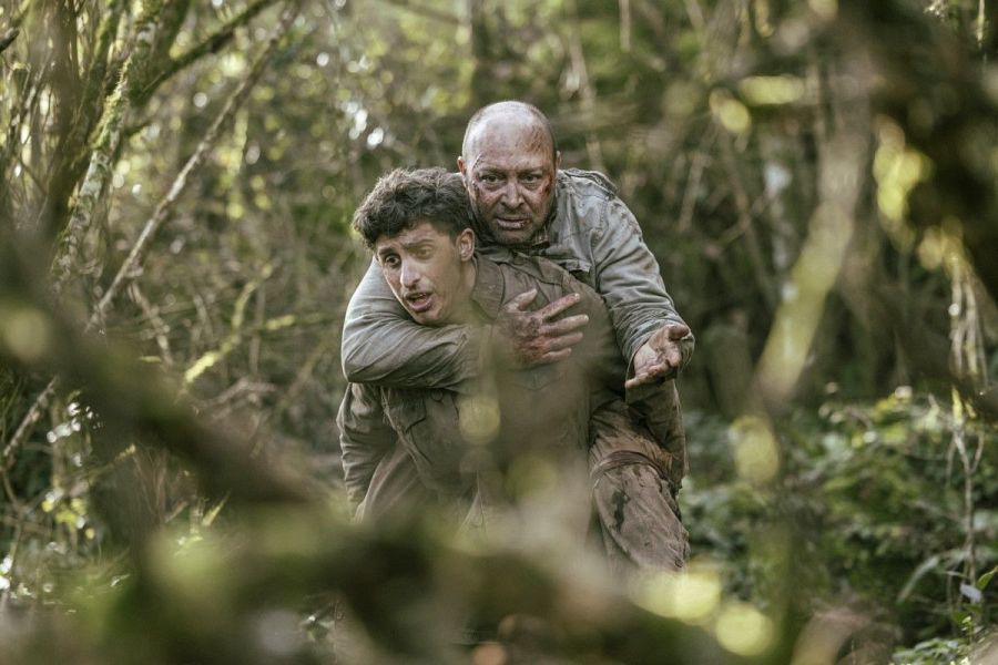 Un joven carga a un hombre mayor a través de un bosque en un fotograma de 'Es el enemigo'.