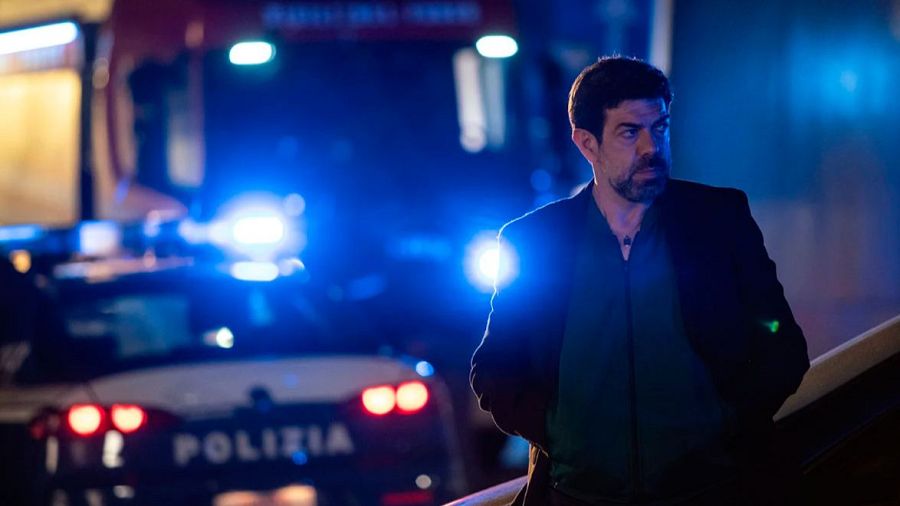 El actor en una escena nocturna con luces de policía al fondo, imagen de la película 'Última noche en Milán'.