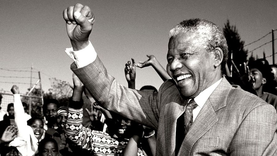 Nelson Mandela levanta el puño en un gesto de triunfo, rodeado de una multitud alegre.