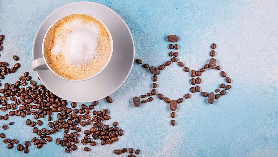 Taza de café y granos de café formando la molécula de cafeína sobre fondo azul.