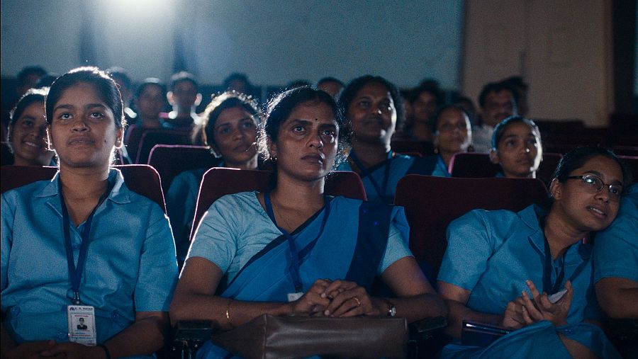 Mujeres con uniformes azules miran atentamente una película en el cine.
