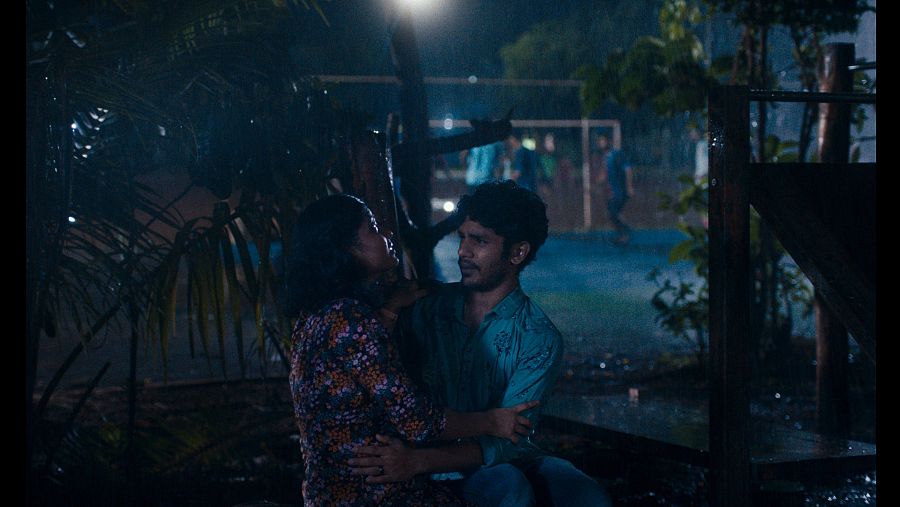 Dos jóvenes abrazados bajo la lluvia en una escena nocturna de 'La luz que imaginamos'.