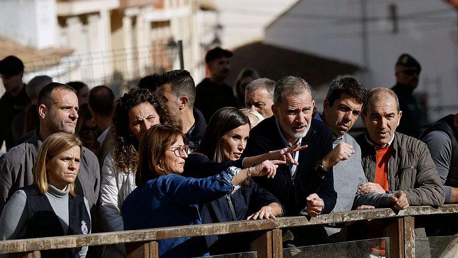 Los reyes Felipe VI y Letizia visitan Chiva y observan algo al otro lado de una valla.