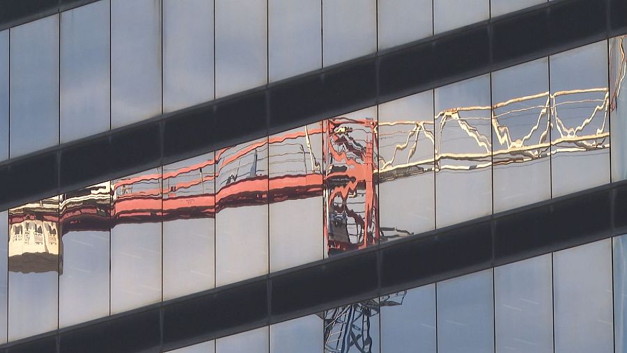 Reflejo distorsionado de una grúa en la fachada acristalada de un edificio.