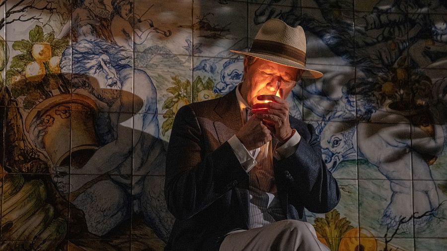 Javier Bardem enciende un cigarrillo en una escena de 'Parthenope', frente a un mural de azulejos.