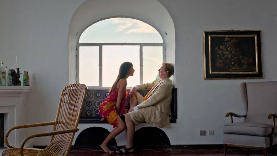 Dos personas conversan en una escena de la película 'Parthenope', sentadas bajo una ventana.