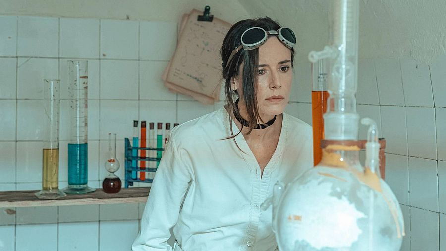 La actriz Pilar López de Ayala, caracterizada como científica en un laboratorio, observa un experimento.
