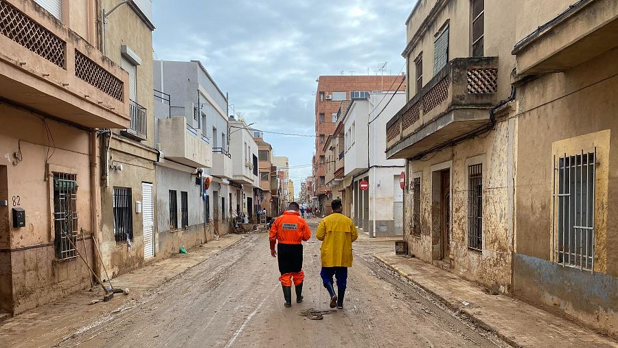 Dos voluntarios caminan por una calle cubierta de barro en Massanassa