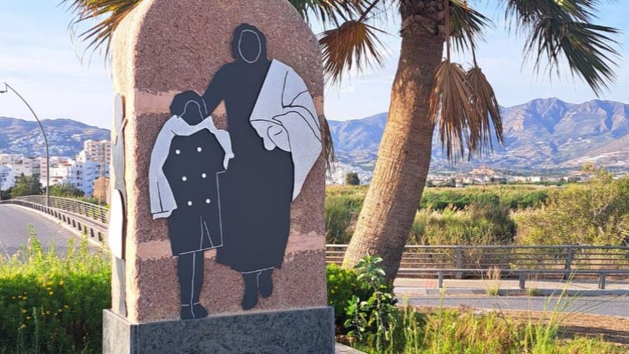 Monumento en Torre del Mar a las víctimas de la Desbandá.  Siluetas recortadas de adulto y niño abrazados.  Fondo con palmera, carretera y edificios.