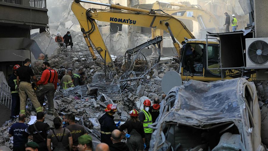 Rescate en Beirut tras un desastre.  Rescatadores buscan víctimas entre escombros, usando excavadoras y camillas.