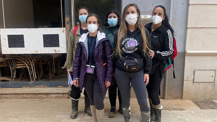 Brigada de la Asociación Alanna: cinco mujeres con mascarillas y ropa de abrigo frente a un edificio con sillas apiladas en su interior.