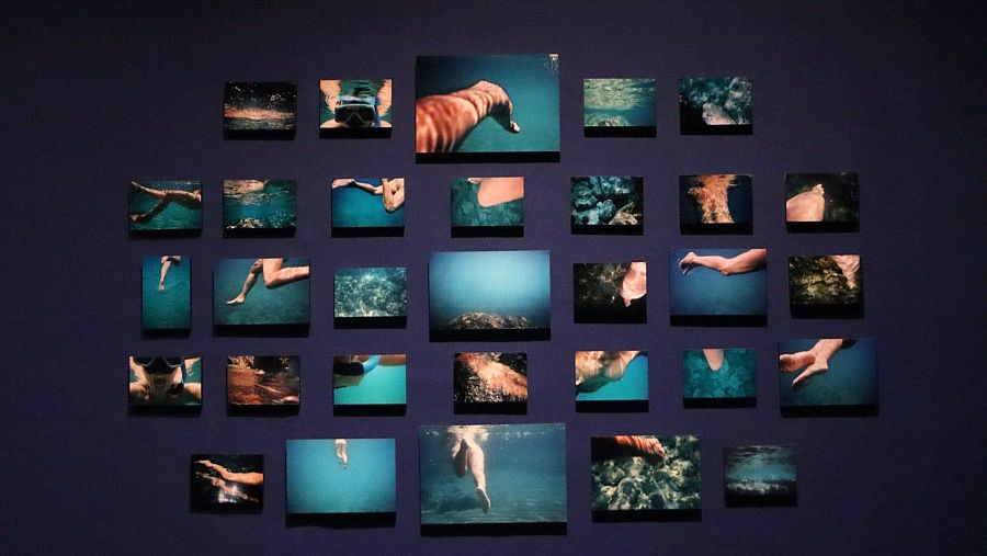 Fotografías de Mari Chordà (2011) mostrando partes del cuerpo sumergidas en agua, dispuestas en cuadrícula sobre pared azul. Obra titulada 
