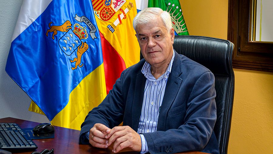 Alpidio Armas, presidente de El Hierro, sentado en su mesa de trabajo con banderas de España, Canarias y El Hierro.