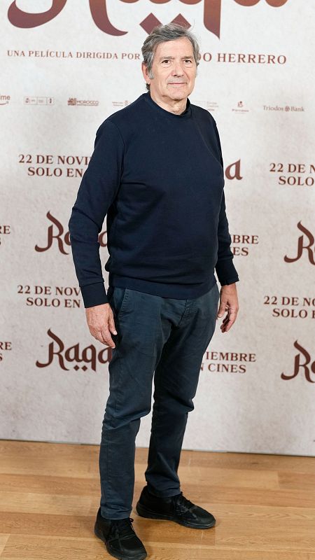 Gerardo Herrero en la presentación de su película 'Raqa'.  Viste jersey azul oscuro y pantalones grises. Cartel promocional visible al fondo.