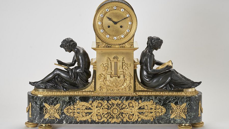 Reloj de sobremesa de 1810 con base de mármol, decoraciones doradas, dos figuras femeninas de bronce y una lira dorada.