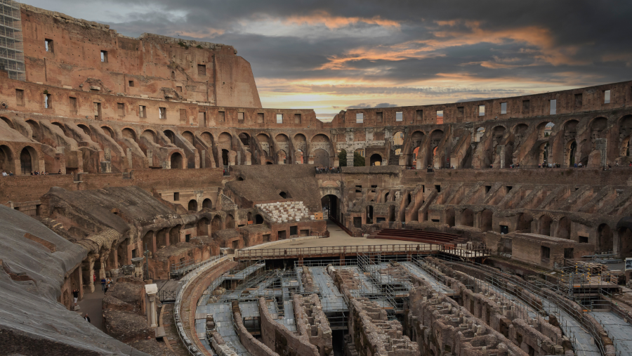 Impresionante vista del Coliseo romano al atardecer, con andamios en la arena y personas en las gradas superiores.