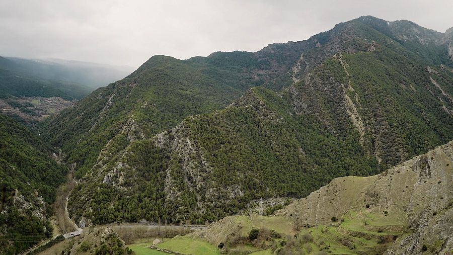 Impresionante vista aérea de un paisaje montañoso con abundante vegetación, zonas rocosas y un camino sinuoso.