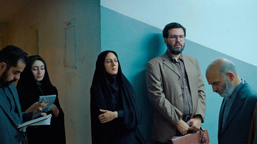 Grupo de personas, posiblemente de la película 'Araña Sagrada', en un pasillo. Dos mujeres con hiyabs y tres hombres; dos parecen tomar notas, uno lleva un maletín.