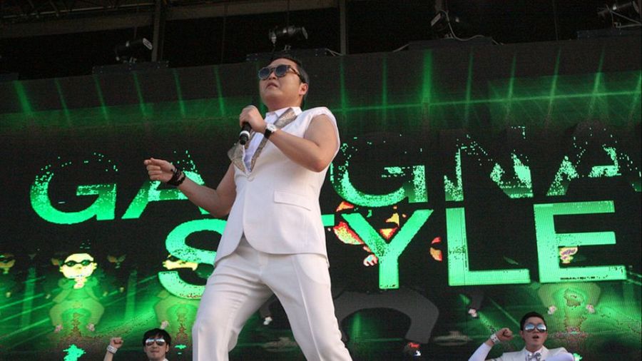 PSY canta y baila 'Gangnam Stule' en un escenario con una pantalla verde que muestra el título de la canción
