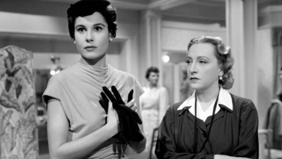 Dos mujeres, una con vestido y guantes negros, la otra con camisa blanca y chaqueta oscura, en una escena de la película 