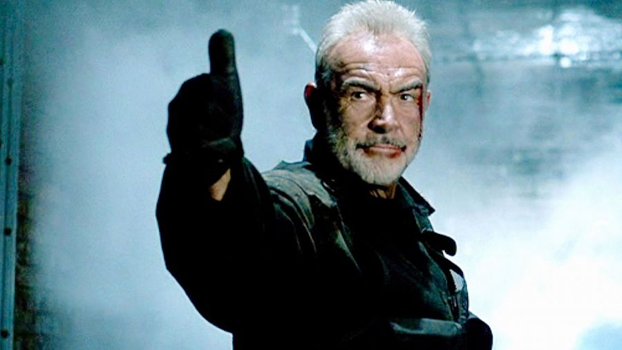 Sean Connery en una escena de 'La Roca', con chaqueta oscura y pulgar arriba. Fondo oscuro y borroso.