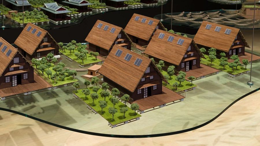 Maqueta de asentamiento con casas de madera y paneles solares, sobre plataformas elevadas y con vegetación. Obra 'Stored in a Jar' de Tiffany Chung.