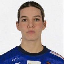 Nicole Wiggins, jugadora de balonmano en los Europeos, luce camiseta azul con detalles rojos y blancos sobre fondo blanco.