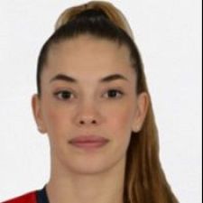 Retrato de Paula Arcos, jugadora de balonmano, con expresión seria. Pelo recogido, camiseta roja y azul. Fondo liso.