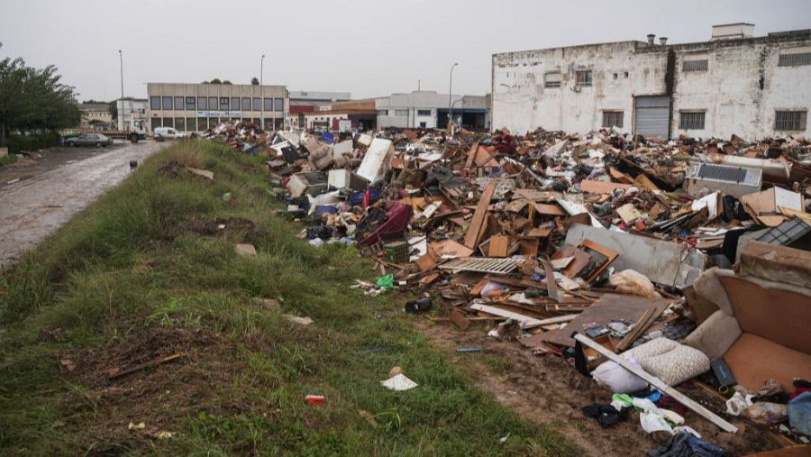 Escombros, muebles rotos y basura cubren una parcela en Beniparell tras la DANA.  Suelo embarrado y edificios al fondo.
