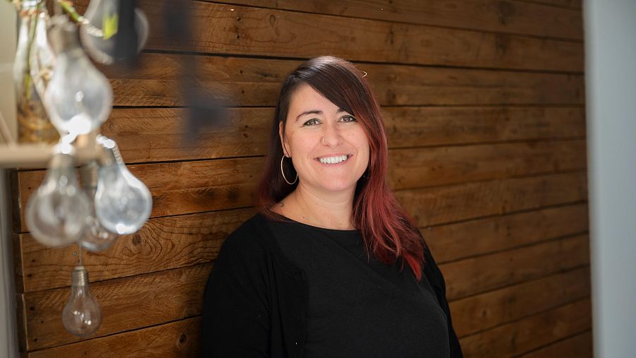 Elenea Crespi, sexóloga, sonríe a cámara. Lleva blusa negra y pendientes grandes. Fondo de madera.