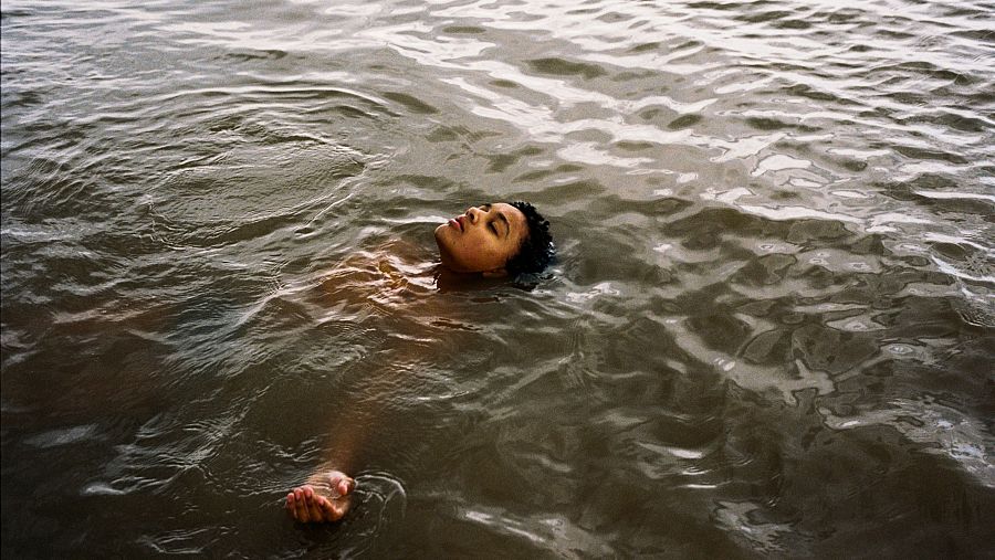 Fotografía de Nykiya Adams flotando en agua oscura y tranquila, parte de la obra 