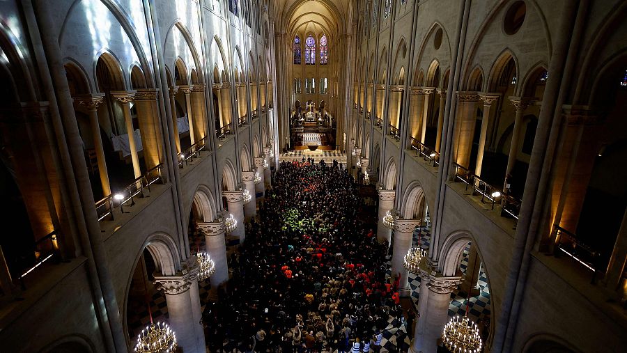 Interior de Notre Dame en París, multitud de personas en la nave central durante una visita presidencial. Arquitectura gótica visible.