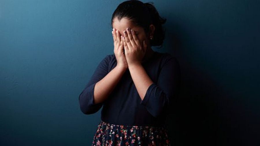 Niña con las manos en la cara, pelo recogido y vestida con camiseta azul y falda estampada.  #Tendencias