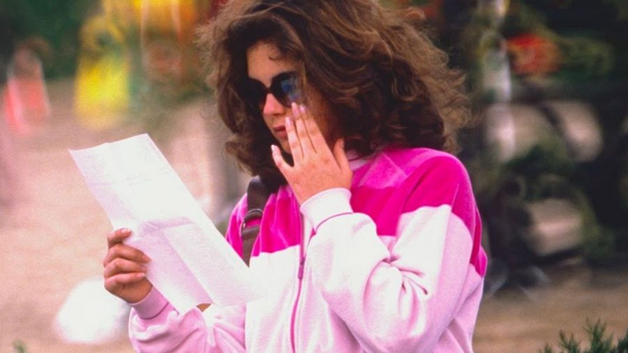 Sonia Martínez, presentadora de TV española de los 80, lee un documento con expresión pensativa. Lleva chaqueta rosa y blanca y gafas de sol.