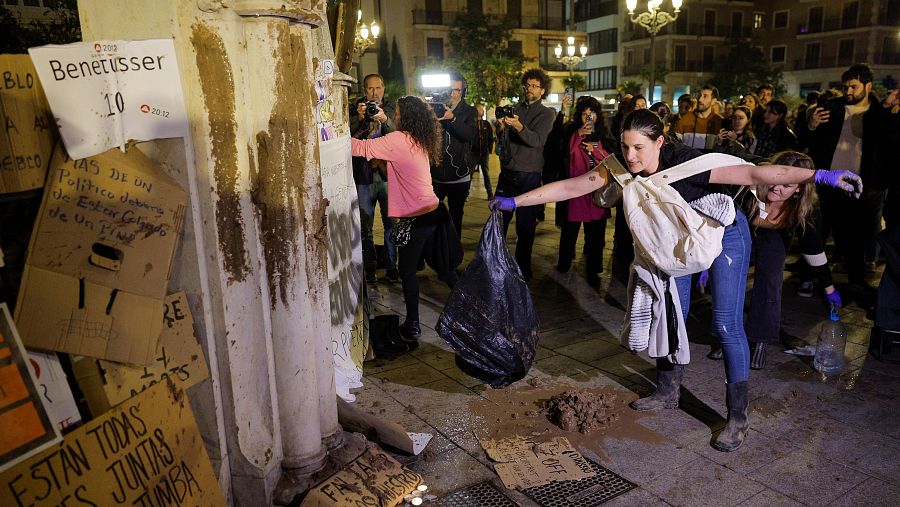 Mujeres arrojan barro en protesta durante una marcha en Valencia.  Se observan carteles y personas grabando la escena con sus teléfonos.