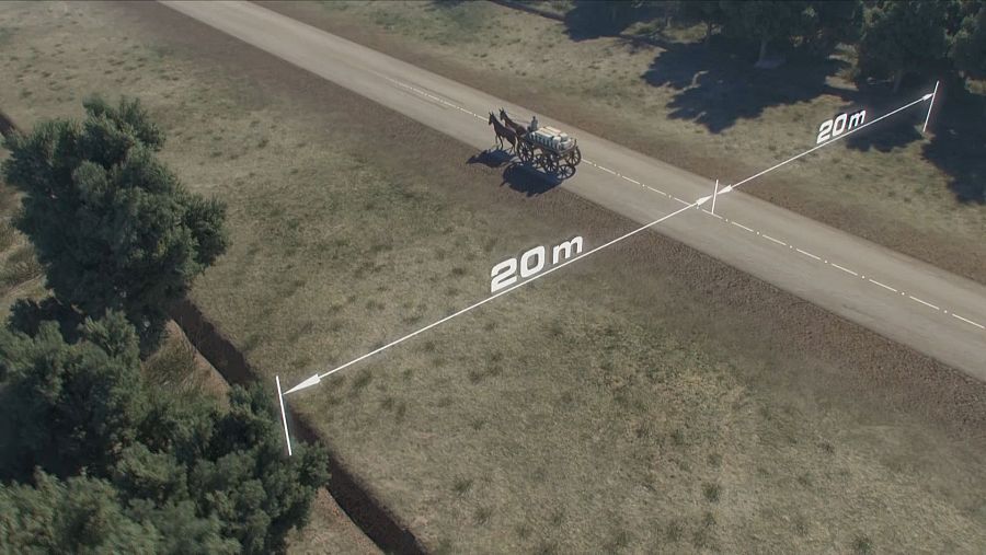 Vista aérea de una calzada de grava y tierra compactada, con un ancho de 20 metros, transitada por un carruaje de dos caballos.  Líneas blancas indican las dimensiones.