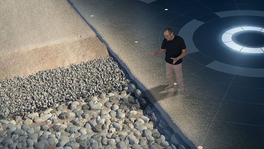 Sección transversal de una calzada romana con sus capas de materiales, señaladas por un hombre.  Imagen de un documental o programa con gráfico circular moderno de fondo.