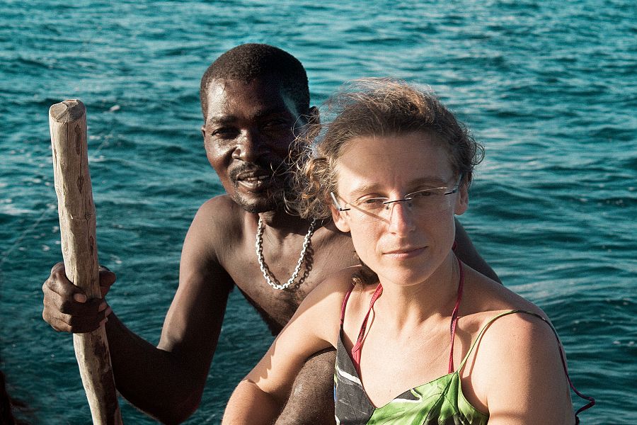 Dos personas en una embarcación sobre agua turquesa. Él, con remo y cadena; ella, con gafas y vestido playero. Ambos miran a la cámara.