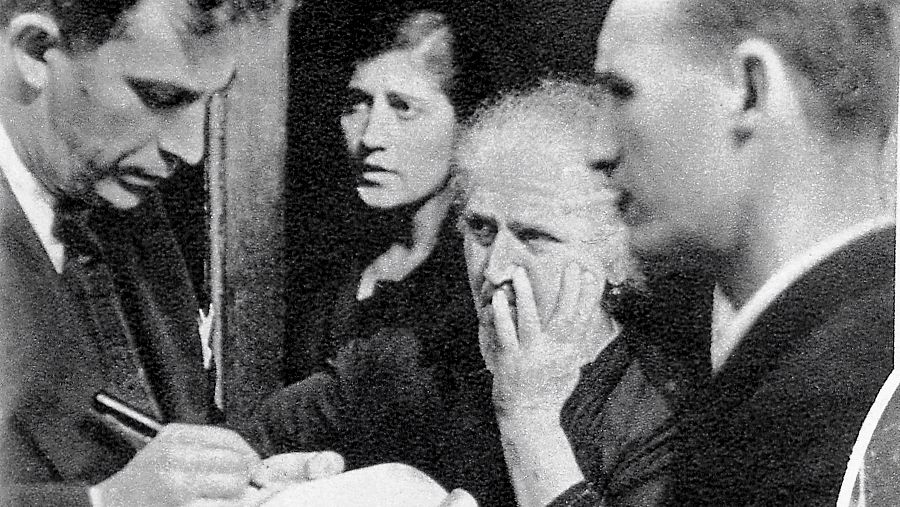 Manuel Chaves Nogales, vestido de traje, firma un autógrafo mientras varias personas le observan atentamente.