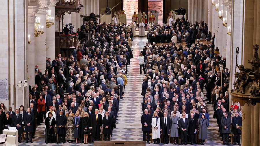 Multitud formal en el interior de Notre Dame durante una ceremonia.  Pasillo central con patrón ajedrezado. Púlpito con equipos de grabación visibles.