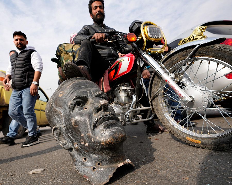 Un combatiente en motocicleta pisa un busto roto del difunto presidente sirio Hafez al Asad en Damasco