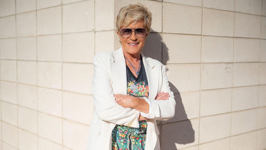 Chelo García Cortés, con gafas de sol y ropa estampada, posa apoyada en una pared blanca.  Imagen que acompaña a un texto sobre su bisexualidad.