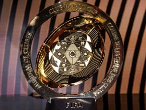 Trofeo dorado circular con base negra, placa central grabada y aro con el nombre del torneo en tres idiomas.  Inscripción 