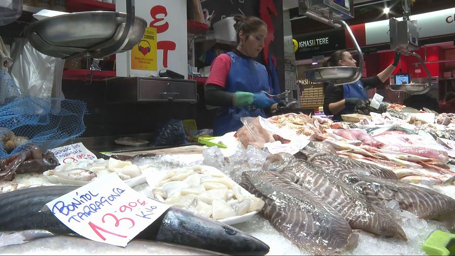 Puesto de pescado en mercado cubierto.  Mujer con guantes azules atiende, pescados sobre hielo, cartel con precio del bonito.  Escasa variedad por huelga.