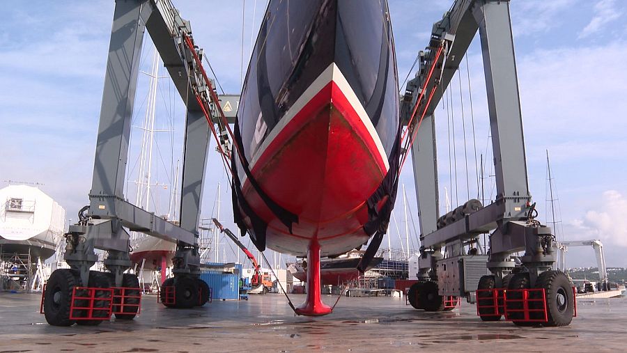 Grúa pórtico elevando un velero rojo y negro en un astillero.  El barco parece sometido a tareas de mantenimiento.